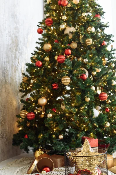 Weihnachtsbaum mit roten und goldenen Kugeln und goldenen Lichterketten in einem hellen Raum. — Stockfoto