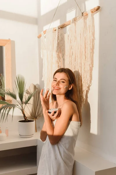 Счастливая молодая женщина наносит крем в ванной. Кожа, концепция лечения. Портрет крупного плана — стоковое фото