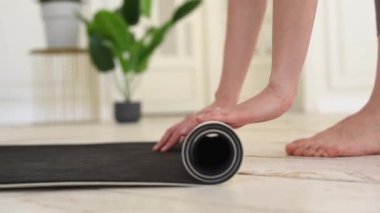 Evde ya da spor salonunda egzersiz yaptıktan sonra gri yoga ya da spor paspası katlayan genç kadınların yakın çekimi. Yoga, spor, sağlıklı yaşam tarzı konsepti