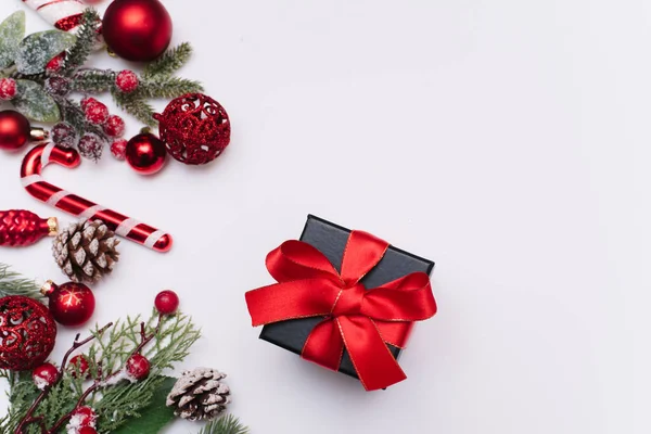 Ramas de abeto con decoraciones rojas navideñas y bolas alrededor de un regalo negro con lazos rojos sobre un fondo blanco con espacio de copia para texto. Fotos de stock libres de derechos
