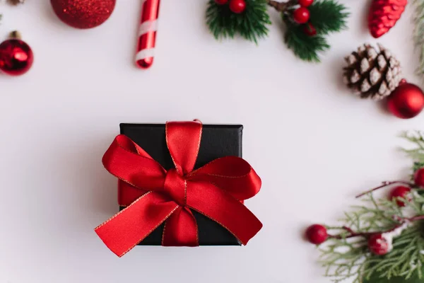 Vánoční dárek s červenou mašlí na bílém pozadí s jedlovými větvemi a dekoracemi na bílém pozadí. Pohled shora. — Stock fotografie