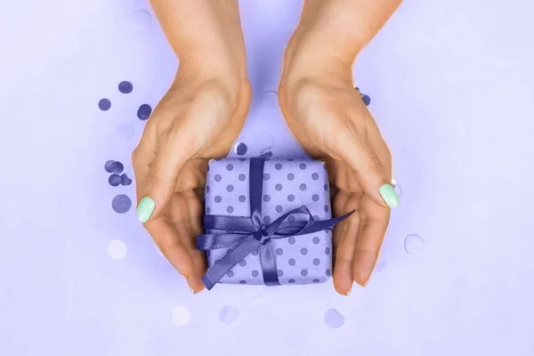 Mãos femininas com manicure pastel azul segurando um presente com um arco em um fundo roxo muito peri 2022. O conceito do feriado, presentes, surpresas, aniversário, ano novo e Natal — Fotografia de Stock