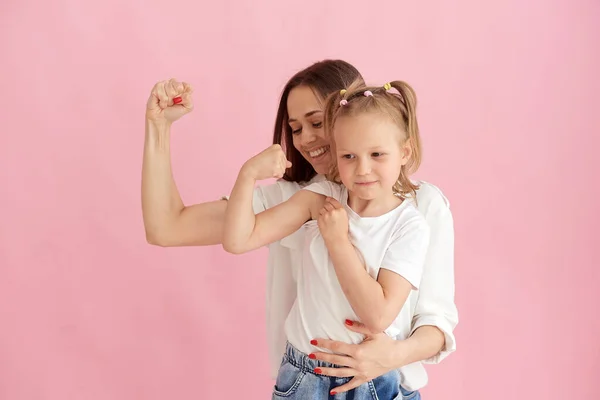 Funny family on the background of a bright pink wall. Mother and her daughter little girl having fun, showing that the strength of the muscles. Woman power, feminism Imágenes de stock libres de derechos