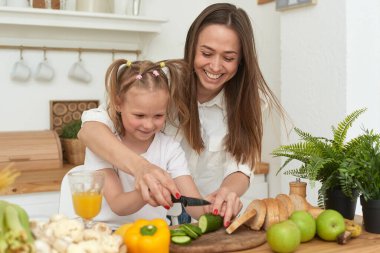 Mom and daughter are preparing salad together in their kitchen. Spending time with your family. Proper nutrition of the child