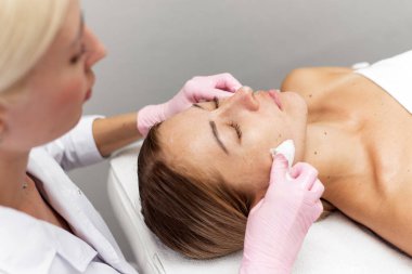 Relaxed young woman resting on a couch while the beautician massages her face and cleanses her skin. Spa treatments. Anti aging