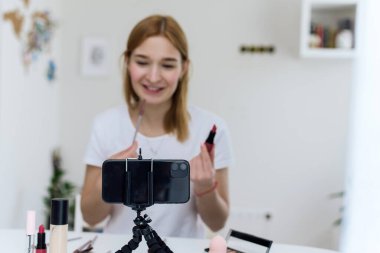 Kadın video blogcusu yüzüne nasıl kozmetik uygulanacağını gösteriyor. Hayvansal olmayan kozetikler hakkında konuşmak için harika bir kadın etkileyicidir.