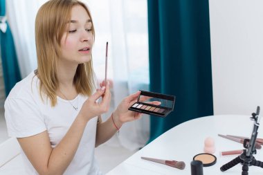 Güzellik kıyafetleri, makyaj dersleri. Mutlu kadın vlogger, sosyal medyada internet kanalı için telefonda video akışı kaydederken kozmetik ürünleri gösteriyor. güzellik blogu kozmetik hakkında