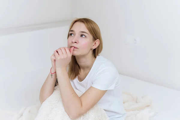 Uma jovem se senta na cama, se preocupa e morde as unhas. Mulher casual preocupado sentado em sua cama no quarto — Fotografia de Stock