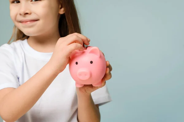 Una niña pone una moneda en una alcancía. El concepto de enseñar a los niños finanzas personales y ahorro. Fotos de stock libres de derechos