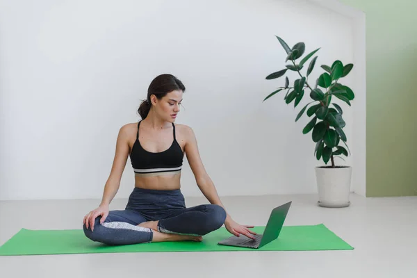 Молода жінка займається спортом і йогою вдома, використовуючи ноутбук. Реклама для курсів йоги . — стокове фото