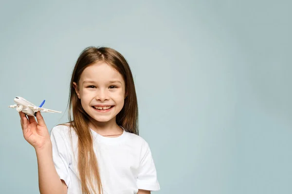 Niña sonriendo mientras sostiene un avión falso sobre un fondo azul y mirando a la cámara. Concepto de turismo y viajes. Copiar espacio — Foto de Stock