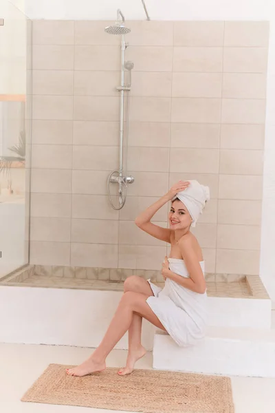 Eine junge lächelnde Frau pflegt nach dem Duschen Haut und Haare. Wellness-Behandlungen zu Hause, Hautpflege. — Stockfoto