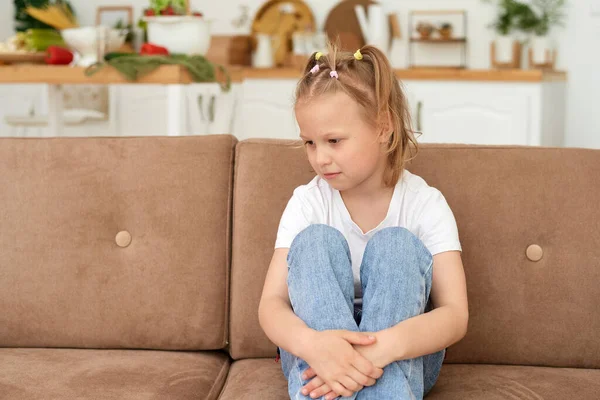 A little girl is sitting on the couch at home and is sad. Domestic violence and abuse concept — Φωτογραφία Αρχείου