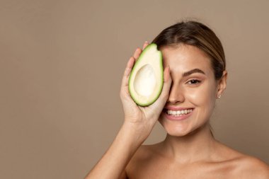 Elinde yarım sulu avokado tutan gülümseyen bir esmer. Doğal malzemelerden kozmetik konsepti