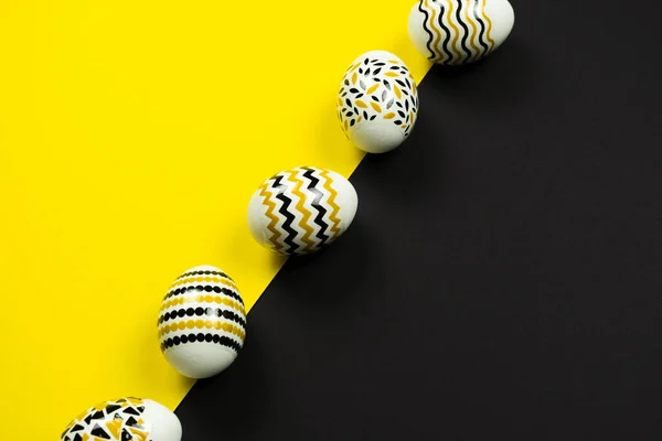 Huevos dorados, negros y blancos con un patrón geométrico sobre un fondo amarillo y negro. Vista desde arriba. Tarjeta de Pascua con espacio de copia para texto. — Foto de Stock