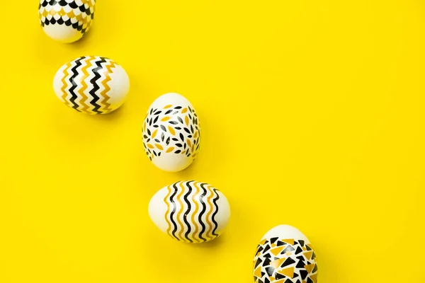 Huevos dorados, negros y blancos sobre un fondo amarillo. Vista desde arriba. Tarjeta de Pascua con espacio de copia para texto. Imagen de archivo