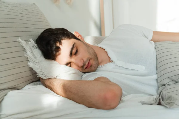 Πλευρική άποψη ενός νεαρού άντρα που κοιμάται στο κρεβάτι στην κρεβατοκάμαρα. Η έννοια της ειρήνης. — Φωτογραφία Αρχείου