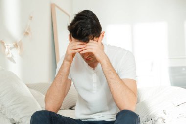Baş ağrısı olan genç bir adam, yatakta hasta yatıyor. İnsan endişelenir, sorunları düşünür..