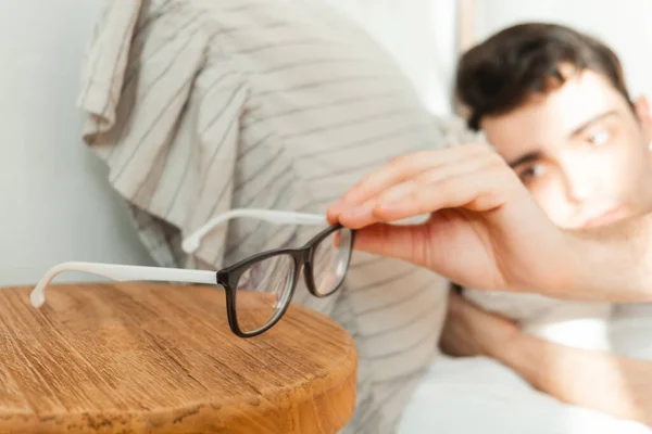 A young man reaches for his glasses after waking up from a dream in bed. — Stock Photo, Image