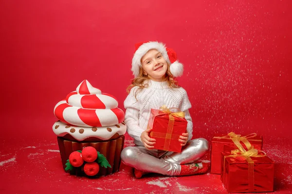 Kleines Mädchen Mit Weihnachtsmütze Auf Rotem Hintergrund Mit Torte Und lizenzfreie Stockfotos