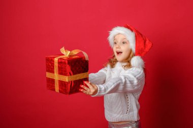 Kırmızı arka planda Noel Baba şapkalı küçük kız pasta ve hediyeyle