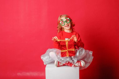 Karnaval yılbaşı kadehlerinde kırmızı arka planda küçük bir kız hediye taşıyor. 