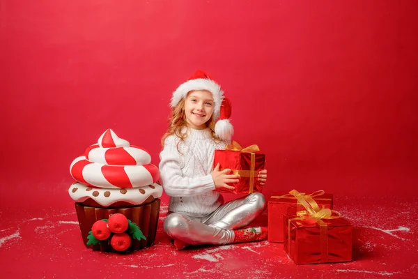 Kleines Mädchen Mit Weihnachtsmütze Auf Rotem Hintergrund Mit Cupcake Und lizenzfreie Stockfotos