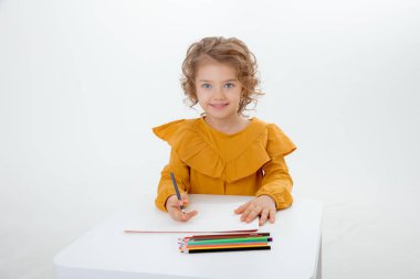 Masada beyaz arka plana izole edilmiş kalemlerle resim yapan küçük şirin bir çocuk.