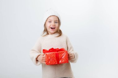Beyaz arka planda izole edilmiş hediye kutularıyla kışlık şapkalı şirin küçük çocuk.