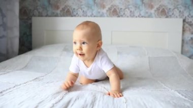 Erkek bebek yatak odasında yatakta emekliyor. Bir bebek beyaz bir yatakta havlamaya başlıyor.