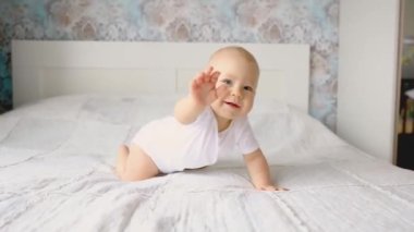 Erkek bebek yatak odasında yatakta emekliyor. Bir bebek beyaz bir yatakta havlamaya başlıyor.
