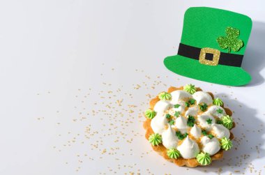 17 Mart 'taki Aziz Patrick Günü konsepti. Lepricon 'un şapkasıyla beyaz arka planda kremalı ve şekerli tart.