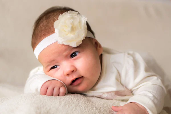 Gyermekkor, anyaság, érzelmek, divat fogalmak - Aranyos mosolygós boldog pufók baba közelről kislány gyönyörű fehér ruha virág fejpánt fején fekvő puha meleg ágy a has otthon — Stock Fotó