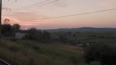 Yüksek hızlı trenden doğa arazisi ve ormanın manzarasına akşamüstü alacakaranlık gökyüzü günbatımı yaz arkaplanında. Kırmızı batan güneş ufukta. Ulaşım, seyahat, demiryolu, iletişim konsepti