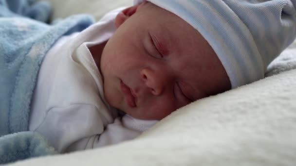 The Close-up Crying Newborn Baby Face Portrait Early Days Sleeping On Tummy Blue White Background. 아이는 모자를 쓰고 인생을 시작 한다. 유아, 출산, 처음 보는 볼링의 순간, 시작하는 개념 — 비디오