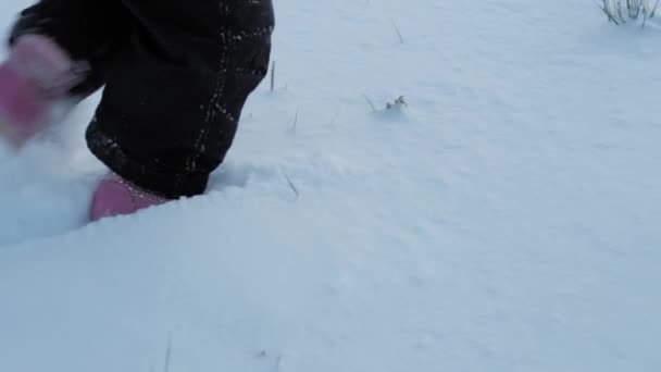 冬、休暇、ゲーム、家族のコンセプト-遅い動きは深い雪の中を赤ちゃんの散歩を閉じます。子供たちは雪の道を歩く。就学前の幼児の子供は寒い季節に雪の中で黒いジャンプスーツを着て — ストック動画