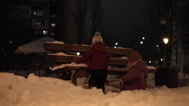 Zima, wakacje, gry, koncepcje rodzinne - środkowy plan autentycznego szczęśliwego przedszkola Małe rodzeństwo dzieci bawią się w parku wieczornym, rzeźbiące śnieżki spadają na śnieg w mroźną pogodę — Wideo stockowe
