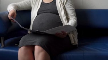 Genç Hamile Koruyucu Maskeli Kadın, hastane için randevu bekleyen koltukta kitap okuyor. Klinikteki jinekoloğu ziyaret et. Muayene Edilmeyi Bekleyen Göbek Sağlığı Kontrolü