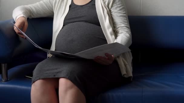 Mulher grávida em medicina leitura de máscara protetora no sofá à espera de nomeação controle médico no hospital. Visite o médico ginecologista na clínica. Examine a barriga expectante Cuidados de saúde Check Up — Vídeo de Stock