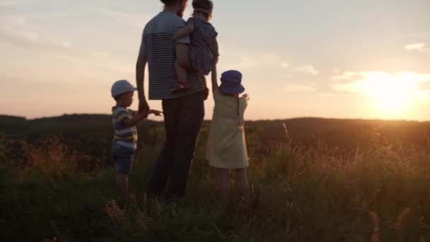 Pessoas no parque. feliz caminhada familiar no campo. pai com muitas crianças no topo da montanha em grama alta antes do pôr do sol. pais e crianças divertidas olhar para a distância. verão, paternidade, conceito de infância — Vídeo de Stock