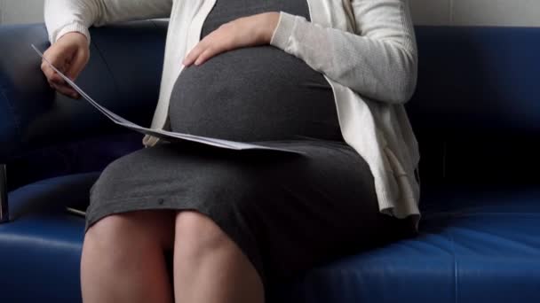 Junge schwangere Frau in der Medizin Schutzmaske Lesen auf der Couch Warten auf Termin Medizinische Kontrolle im Krankenhaus. Besuchen Sie den Frauenarzt in der Klinik. Schwangeren-Bauch-Gesundheits-Check — Stockvideo