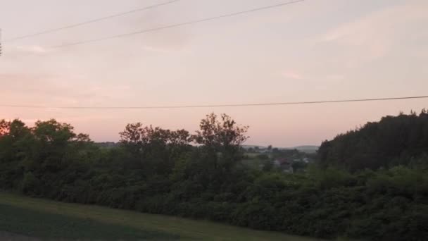 Vista da janela de trem de alta velocidade na paisagem da bela natureza campo selvagem e trilhos ferroviários florestais no pôr do sol da noite em fundo de verão. Transporte, viagens, ferrovia, conceito de comunicação — Vídeo de Stock