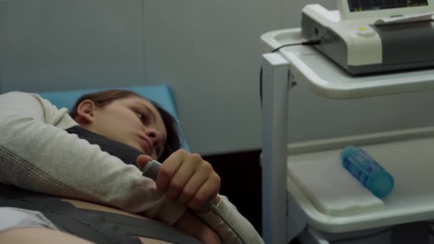 Молода вагітна жінка на лікарняному дивані під час медичного контролю кардіотомографії. Відвідайте гінеколога доктора в клініці консультанта з питань вагітності. Перевірка очікуваного живота дитини здоров'я матері Ознайомтеся — стокове відео
