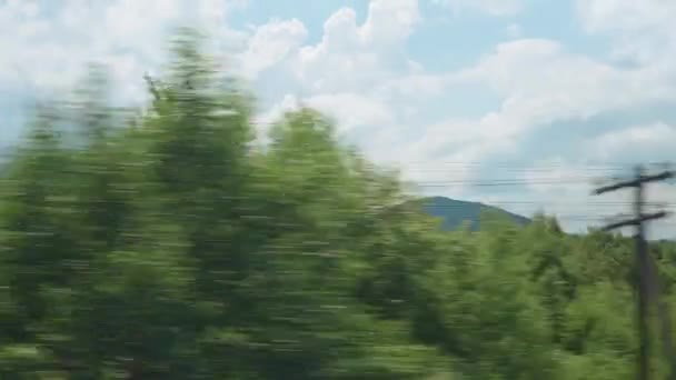 Uitzicht vanuit het raam van de hogesnelheidstrein op landschap van prachtige natuur wild veld en bergen bos op bewolkt schone zonnige dag in de zomer achtergrond. Vervoers-, reis-, spoorweg- en communicatieconcept — Stockvideo