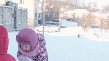 Kış, tatil, oyunlar, aile konsepti ağır çekimde iki mutlu anaokulu çocuğu, şapka ve eldiven takmış iki çocuk ve annemle el ele kar kusuyorlar. Soğuk mevsimde parkta açık havada