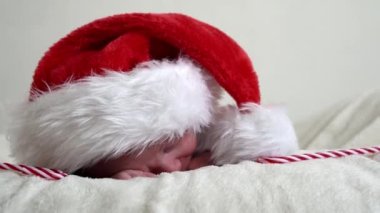 Mutlu noeller ve mutlu yıllar, bebekler, çocukluk, tatil konsepti - yakın plan hayatın ilk günleri yeni doğan üzgün bebek Noel Baba 'da kırmızı şapkalı, beyaz arka planda şeker kamışı olan