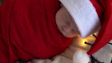Yeni doğan bebeğin ilk portresi beyaz çelenk arka planında kırmızı beze sarılı, Noel Baba şapkalı komik uyuyan bebek. Mutlu Noeller, Mutlu yıllar, Bebek, Çocukluk, Kış Konsepti