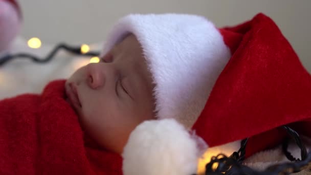 "Close Up Portrait First Days of Life Newborn Cute Funny Sleeping Baby In Santa Hat Wrapped In Red Diaper At White Garland Background" (dalam bahasa Inggris). Selamat Natal, Selamat Tahun Baru, Bayi, Masa kecil, Konsep Musim Dingin — Stok Video