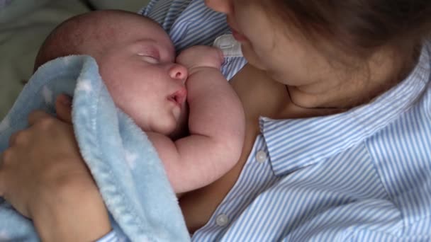 Annelik, çocukluk, aile, bakım, sağlık, annelik konsepti - sıcak mavi battaniyeye sarılı yeni doğmuş bebek anne göğsünün kollarında uyuyor. Anne rahatla, kucağında öpücükle kucağında bebekle evde. — Stok video
