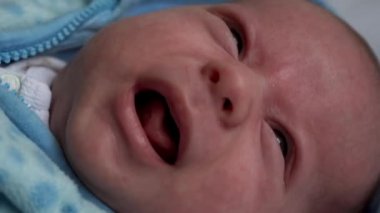 Kameradaki bebeğe bak. Yakın çekim. bebek, çocukluk, ebeveyn sevgisi, duygu konsepti - kahverengi gözlü tombul bebeğin ağlayan, mavi ceketli, uyanık bebek ağlaması evde yatakta yatıyordu.